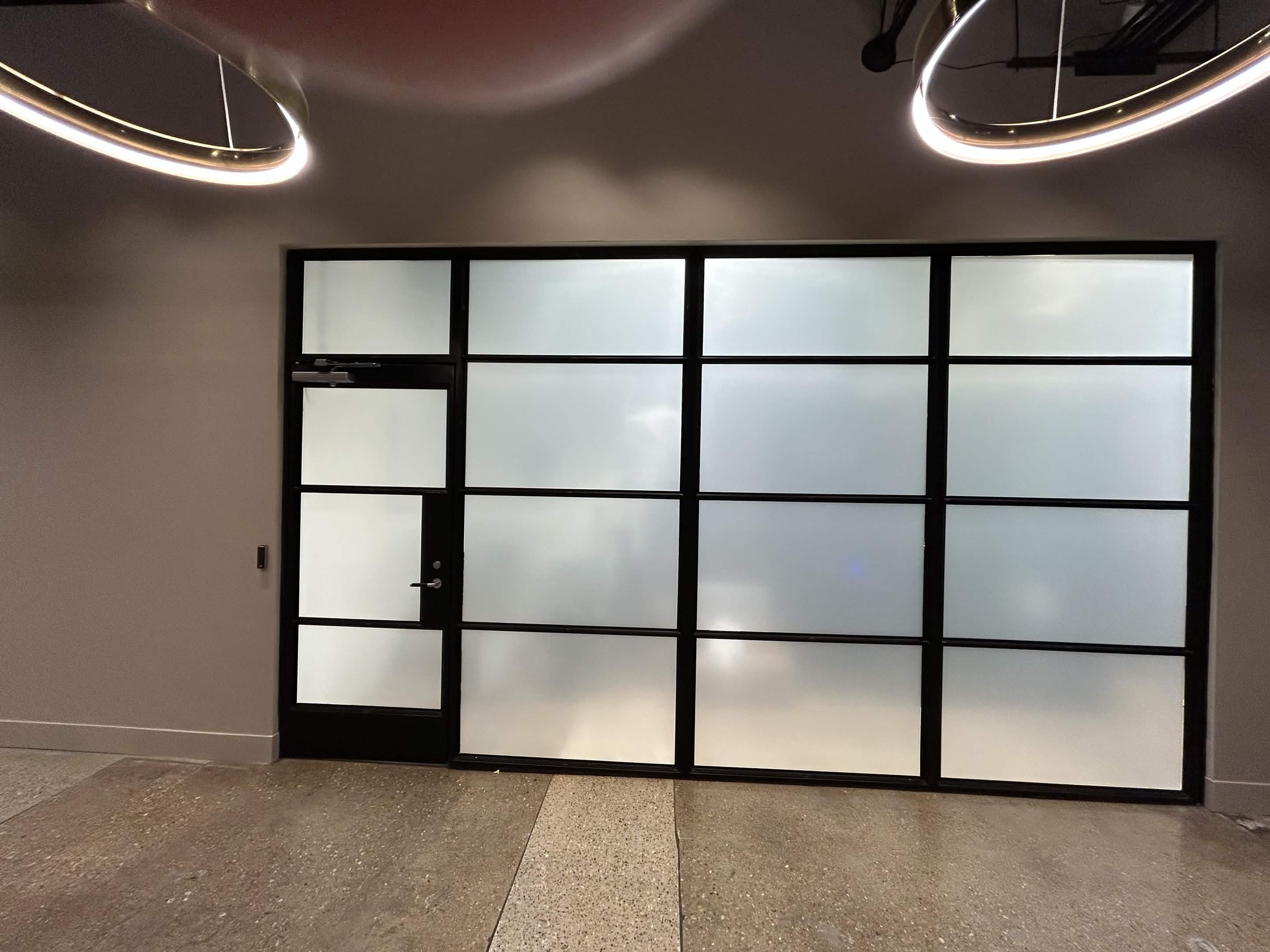 Commercial interior frosted glass partition wall with black metal framing and privacy film